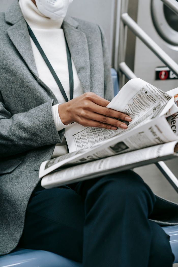Services Crop anonymous black female entrepreneur in elegant outfit and medical mask reading newspaper while riding train