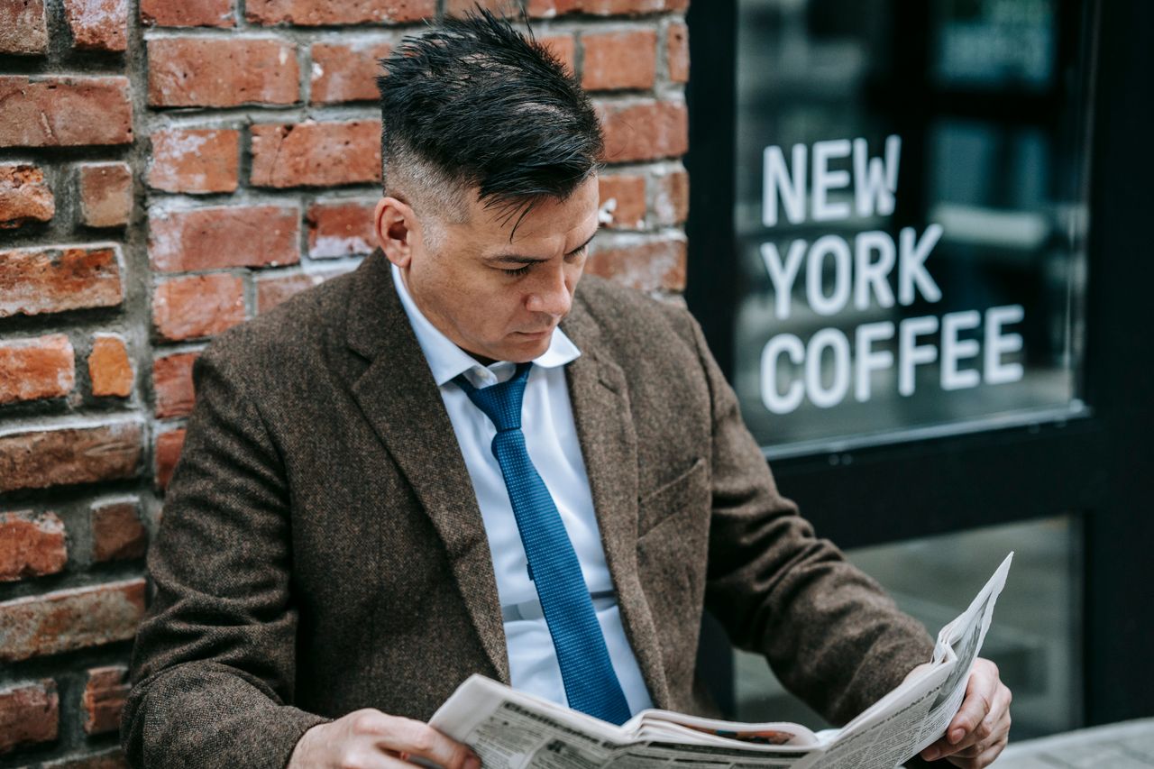 Services Man in formal attire reading a newspaper outside New York coffee shop.